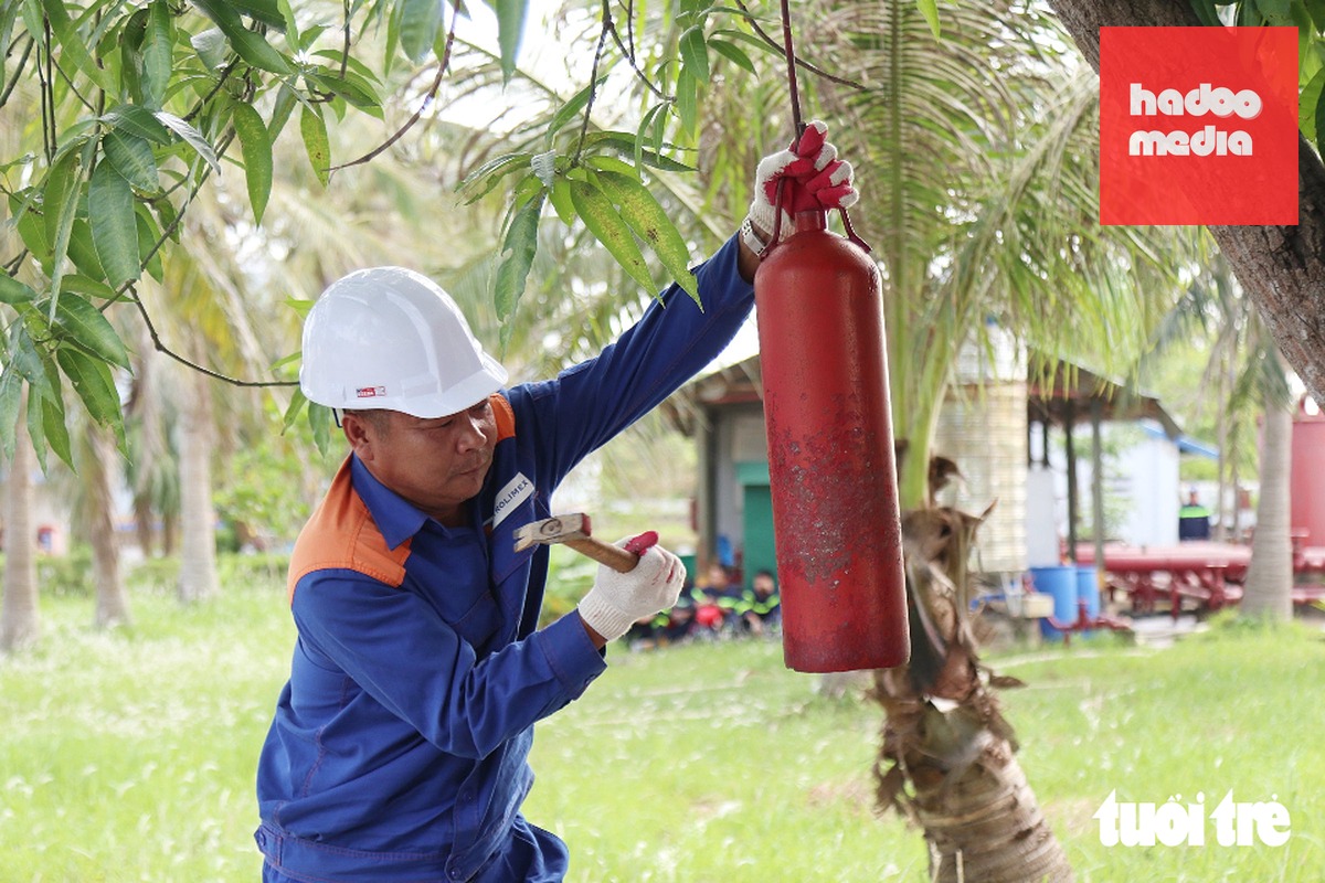 Tình huống giả định bắt đầu vào lúc 8h30 dưới thời tiết dông sét. Hệ thống tiếp địa chống sét của cụm bể chứa đang bảo dưỡng kỹ thuật thì bị sét đánh trúng bể chứa dầu diesel B16. Cú đánh gây nổ hỗn hợp hơi dầu với không khí, hất văng nắp và rách một phần thành bể. Dầu tràn xuống chân bể bắt lửa bùng cháy dữ dội tạo bức xạ nhiệt cực lớn. Trong ảnh: Nhân viên kho xăng đánh kẻng báo động về sự cố cháy nổ diễn tập - Ảnh: DOÃN HÒA