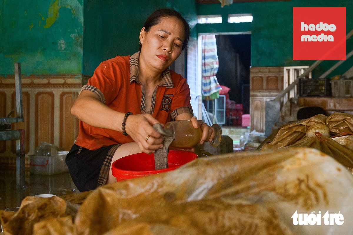 Bà Đàm Vân Anh đang rửa lại số hàng hóa bị dính đầy bùn đất - Ảnh: PHÚC TÀI