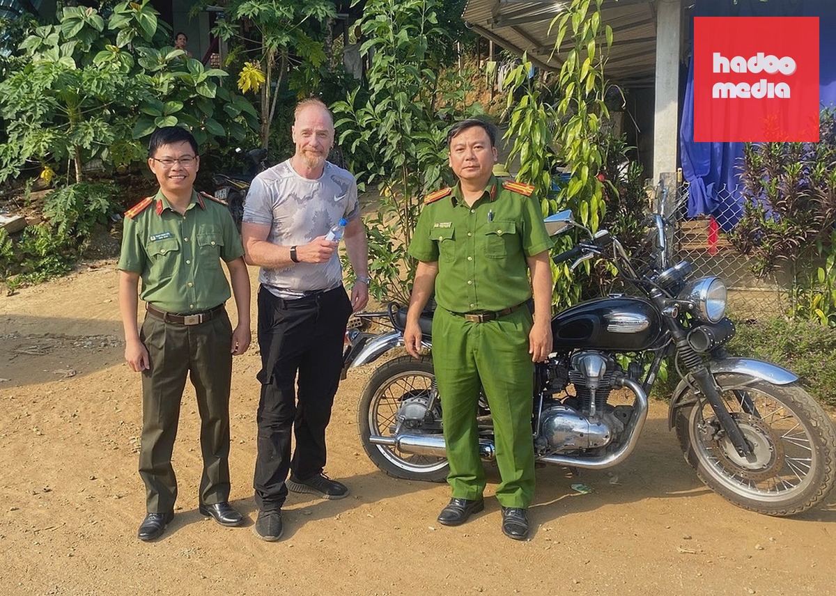 Ông Barry và trung tá Phan Tiến Dũng, Trưởng Công an xã Đặng Thùy Trâm (phải), cùng đại úy Phạm Trung Tiển bên chiếc xe bị thủng lốp bánh sau. Ảnh: Công an xã Đặng Thùy Trâm