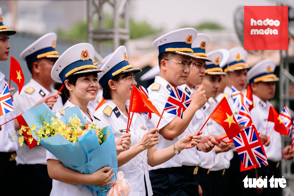 Các đại biểu Quân đội Nhân dân Việt Nam vẫy cờ hai nước Việt Nam - Anh chào đón tàu Hải quân Anh cập cảng Nhà Rồng trưa 22-10 - Ảnh: THANH HIỆP